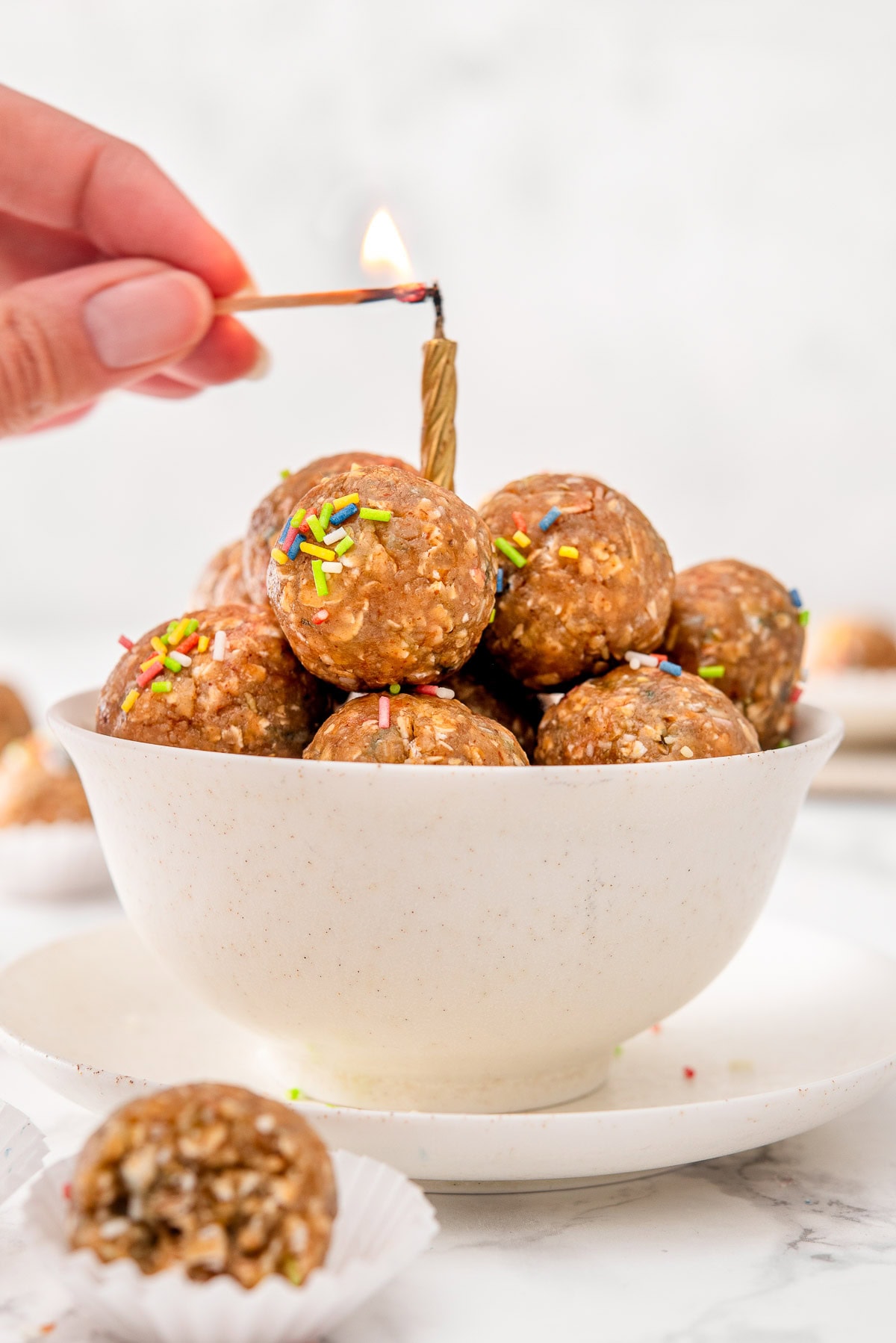 A person lighting up a candle over birthday cake protein balls in a bowl.