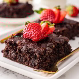Healthy brownies garnished with strawberries on a plate with a fork.