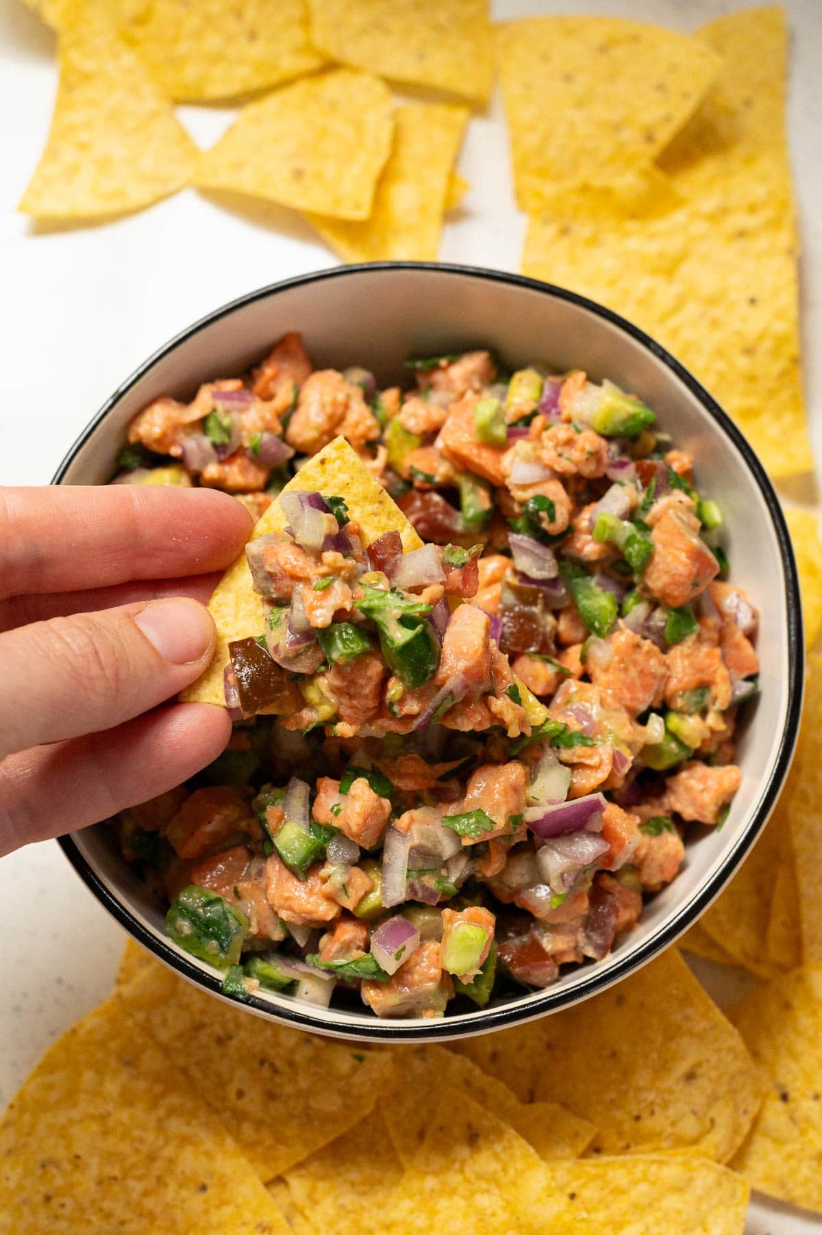 Person scooping salmon ceviche with a tortilla chip.